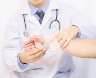 Male doctor putting gauze on young man's hand in clinic, closeup. First aid